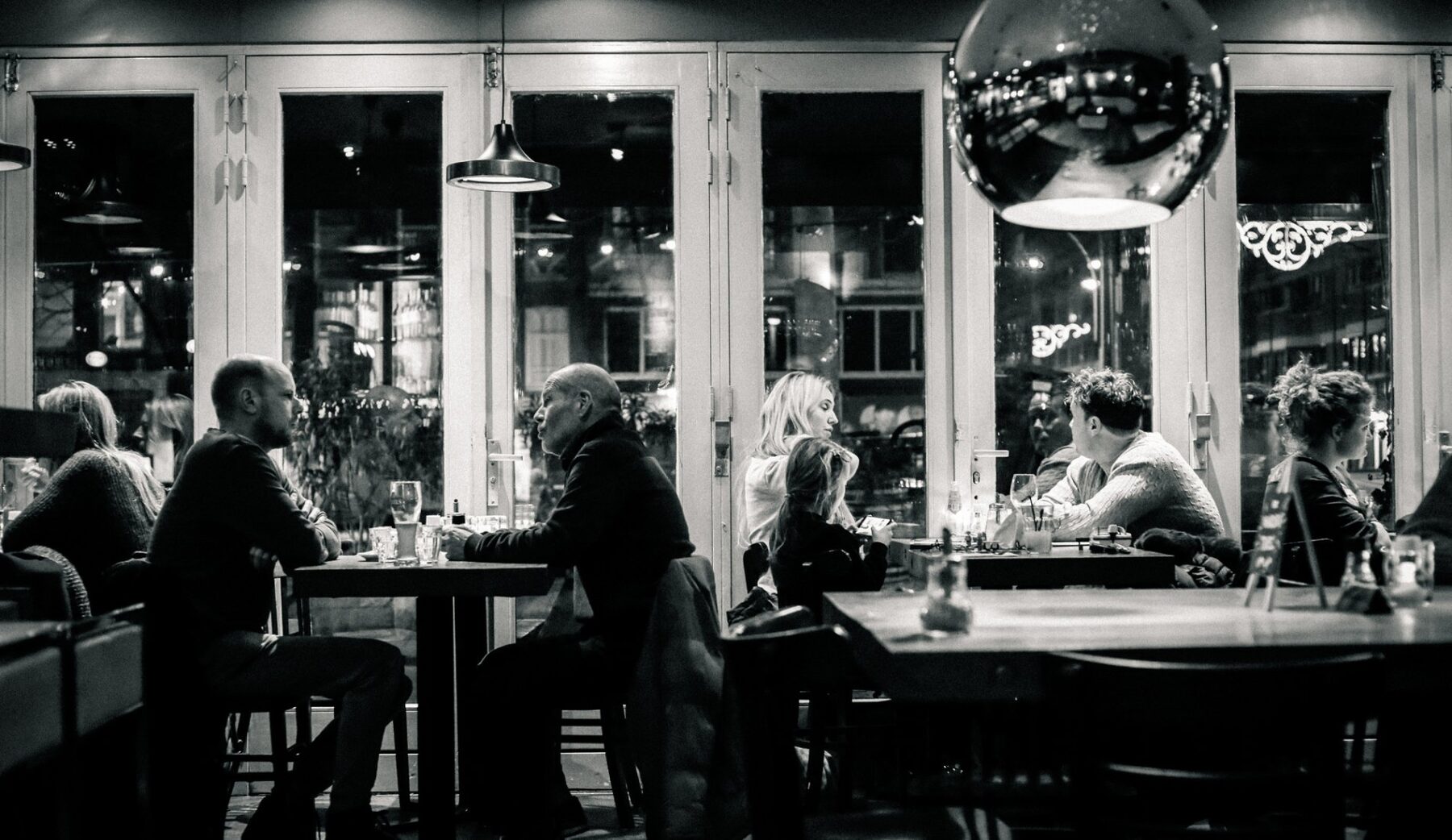 Avondsfeer in Café Nassau met gasten aan tafel bij de grote ramen